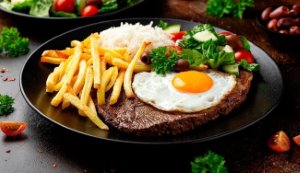 A scrumptious Bife a Cavalo, a traditional Brazilian beef dish topped with a fried egg, served alongside rice and beans.